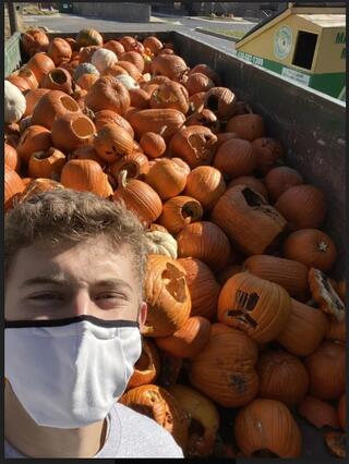 Student with mask in front of a trailer of carved pumpkins